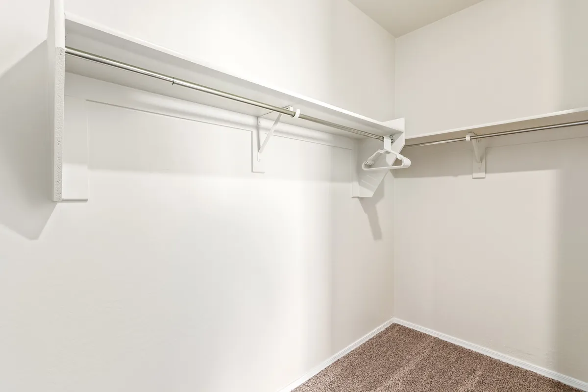 A walk-in closet or storage space featuring a hanging rod, shelves, and a carpeted floor. The scene is neat and uncluttered, ready for organizing clothes, coats, or personal belongings.