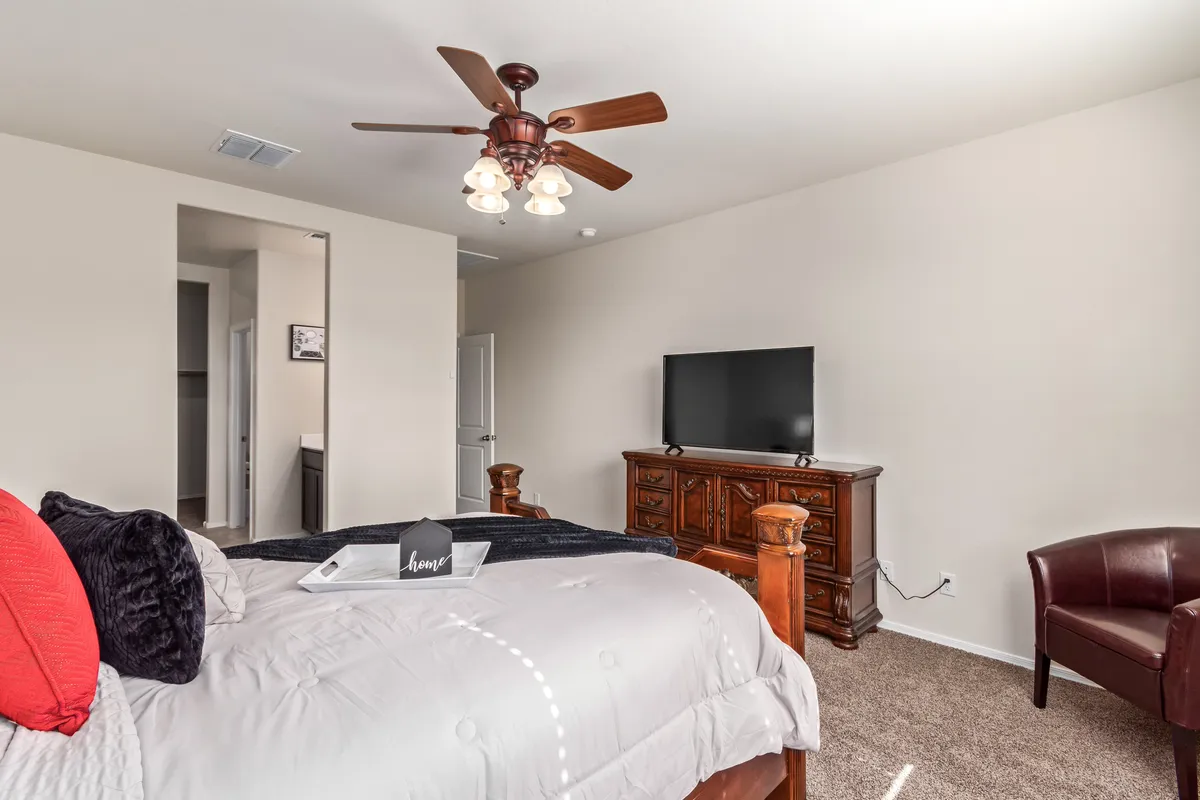 A cozy bedroom features a comfortable bed, dresser, television, and a reading chair, all arranged to foster rest and relaxation after a productive day. The neutral tones and ambient lighting create a calming environment.