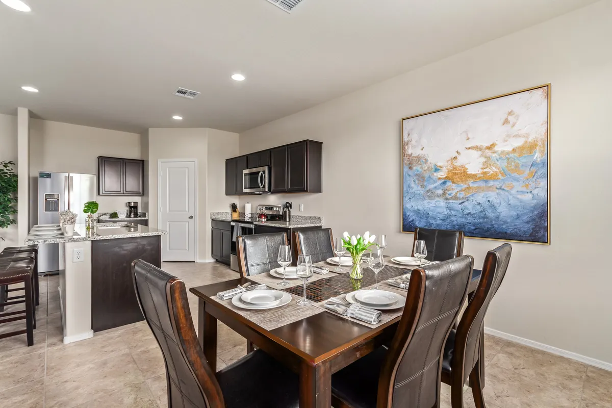 The dining table is beautifully set with dinnerware, backed by elegant wall art and with the kitchen visible in the background. The table seats six, emphasizing the space’s capacity for family meals or celebratory gatherings. Warm lighting and thoughtful decor create a welcoming, festive mood.