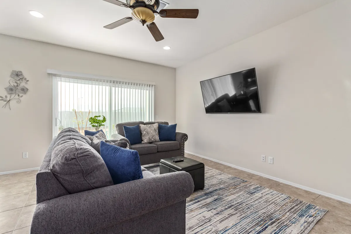 A comfortable living room featuring a plush sofa, a large television, and a window allowing in natural light. Thoughtful, family-friendly decor and wall art contribute to a welcoming atmosphere ideal for families to relax together, celebrate special occasions, and enjoy shared activities.