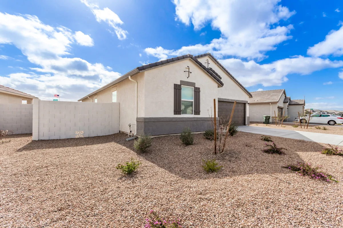 The image features the modern facade of a single-level house with a landscaped front yard and a tranquil blue sky above. The setting evokes a sense of welcoming entry and hints at the possibility of outdoor gatherings, morning coffee in the garden, or relaxing after a day of adventure. The visible covered front porch and inviting garden directly relate to the lifestyle of returning home from desert recreation.