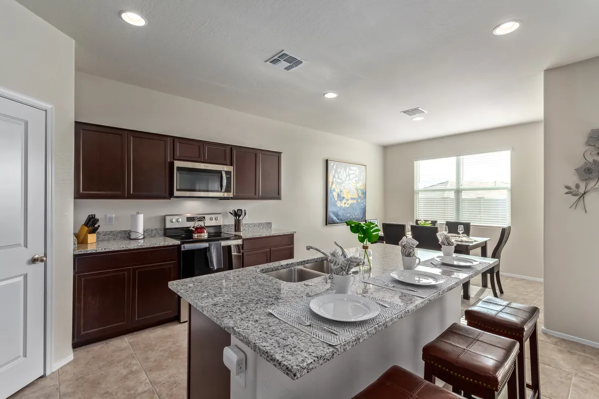 A contemporary kitchen and dining area highlighted by granite countertops, dark wood cabinetry, and modern appliances. The table and chairs offer a comfortable setting for gatherings or multitasking meals.
