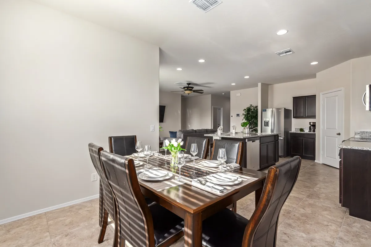 A warm and welcoming interior scene featuring a dining table set adjacent to the kitchen area, with decorative plants adding a touch of greenery. The space is filled with natural light and designed for communal meals or friendly gatherings.