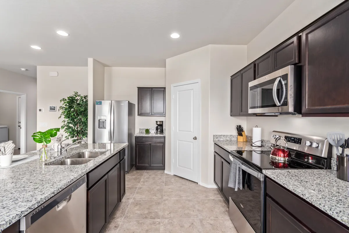 A modern kitchen featuring granite countertops, sleek stainless steel appliances, a spacious kitchen island, and touches of greenery from potted plants. The layout is open and designed for both cooking and entertaining.