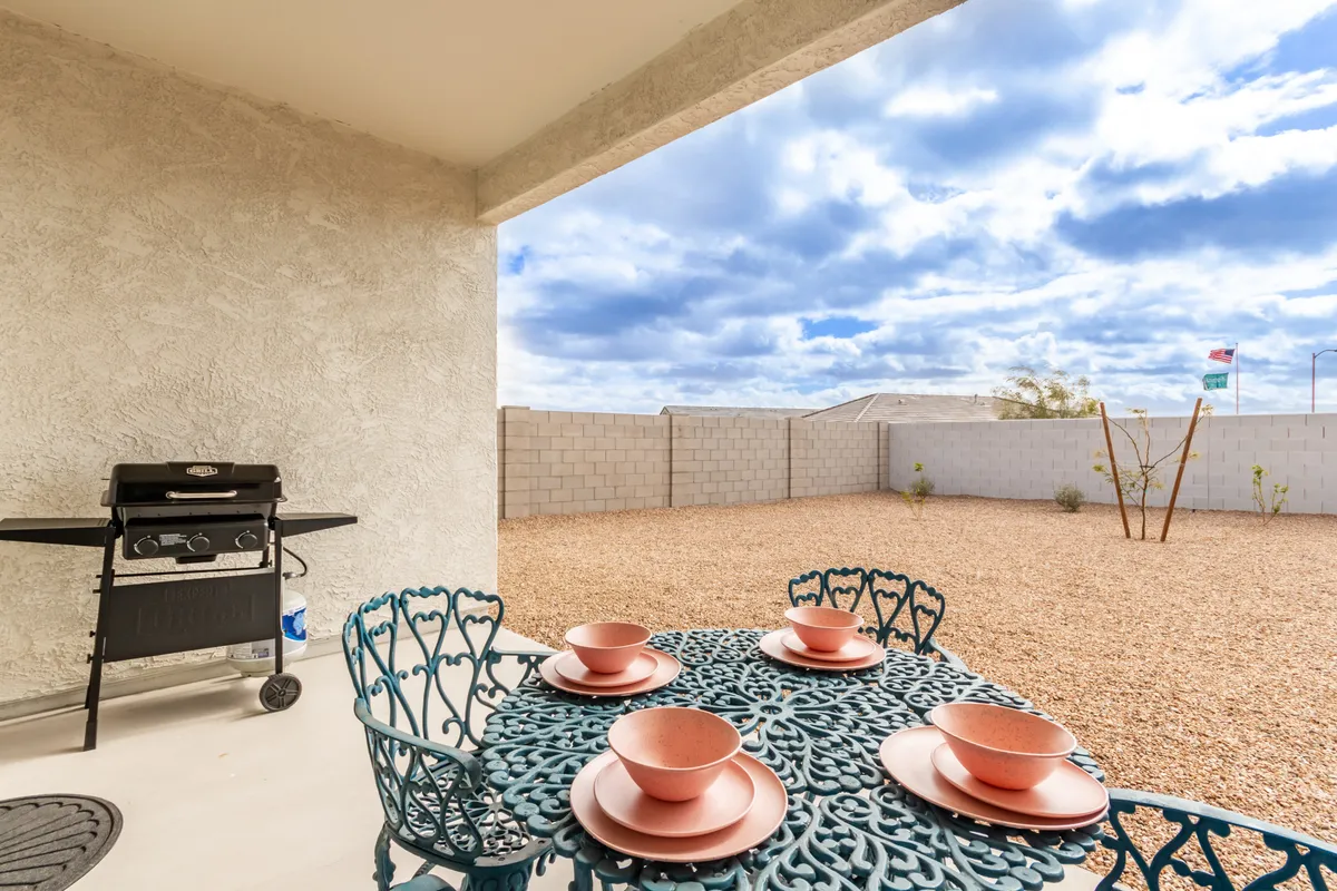This image showcases a covered patio complete with a dining table elegantly set with plates, an outdoor grill nearby, and an expansive, sunlit backyard stretching into the distance. The setup suggests a space designed for both relaxed dining and lively gatherings, framed by the golden Arizona light.