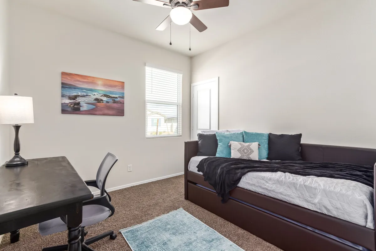 A tranquil flex room set up with a daybed, desk, and wall artwork. The room is brightened by natural light from the window, making it ideal for both productive workdays and restful naps.