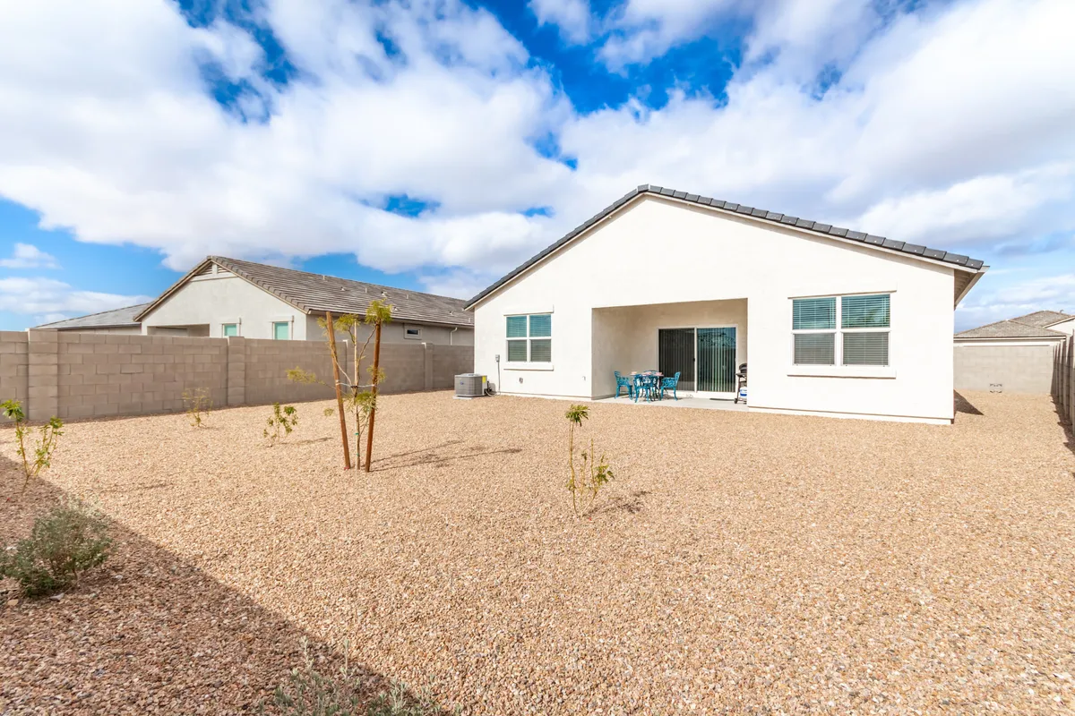 A tranquil backyard view with a focus on the house structure, patio area, gravel yard, and a set of blue chairs arranged for outdoor relaxation. The image evokes a sense of spaciousness and calm, ideal for enjoying the outdoors or hosting gatherings under the open sky.